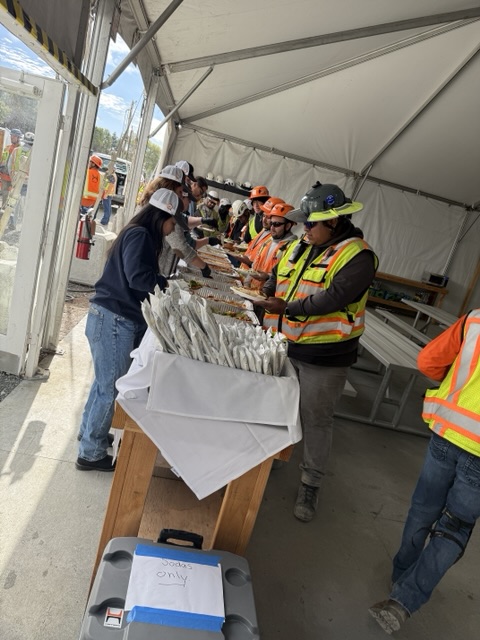 Catering team serving construction workers along a buffet inside a tent